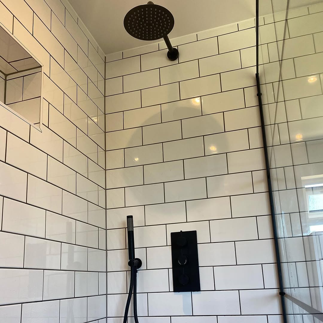 En suite walk-in shower with white metro tiles, black frame screen, and dark hex floor