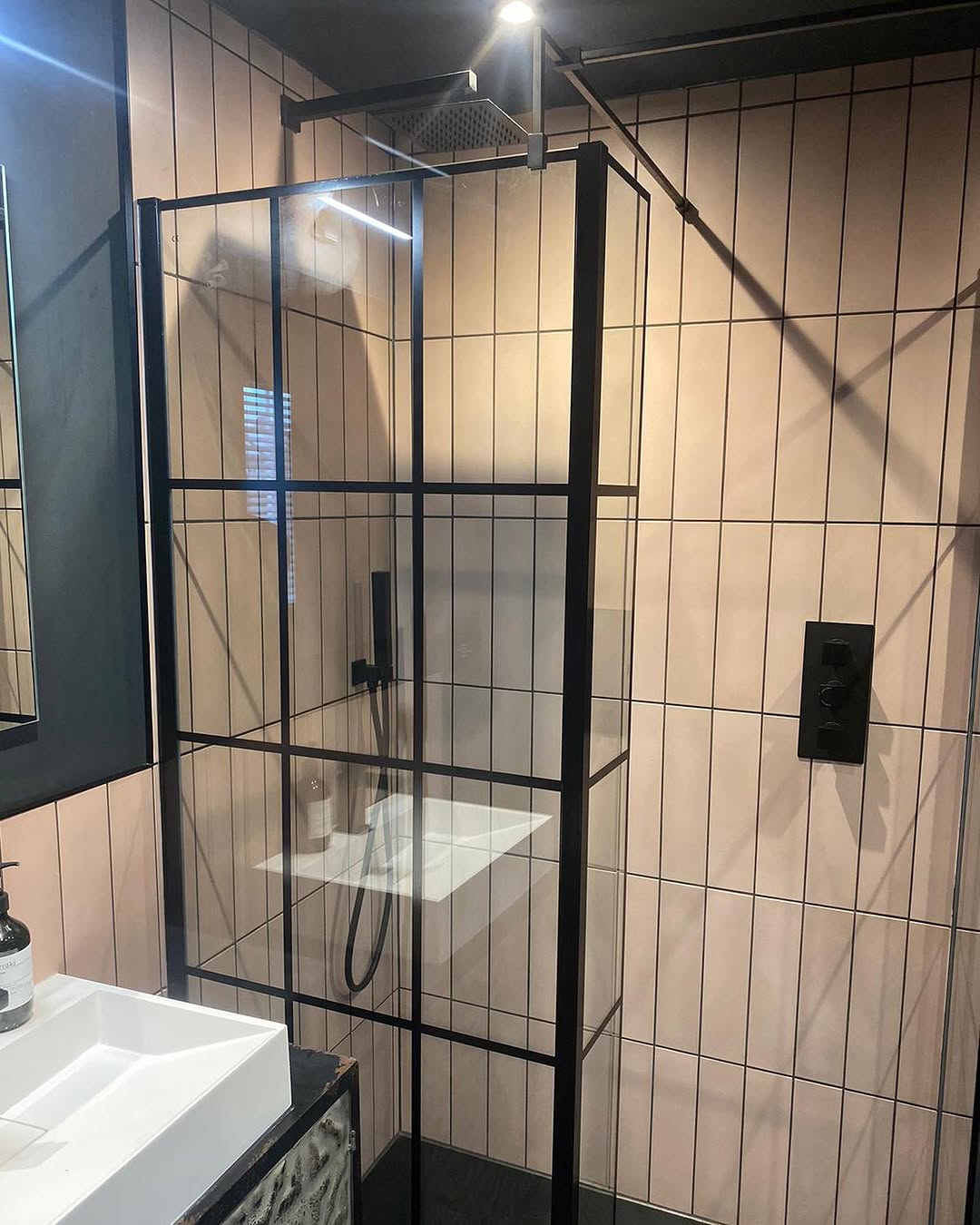 Walk-in shower with black Crittall-style frame, blush vertical tiles, and matt black controls