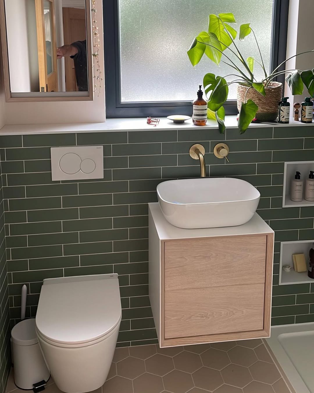 Wide view of the green-tiled bathroom showing floating vanity unit, recessed shelving niches, and bathtub