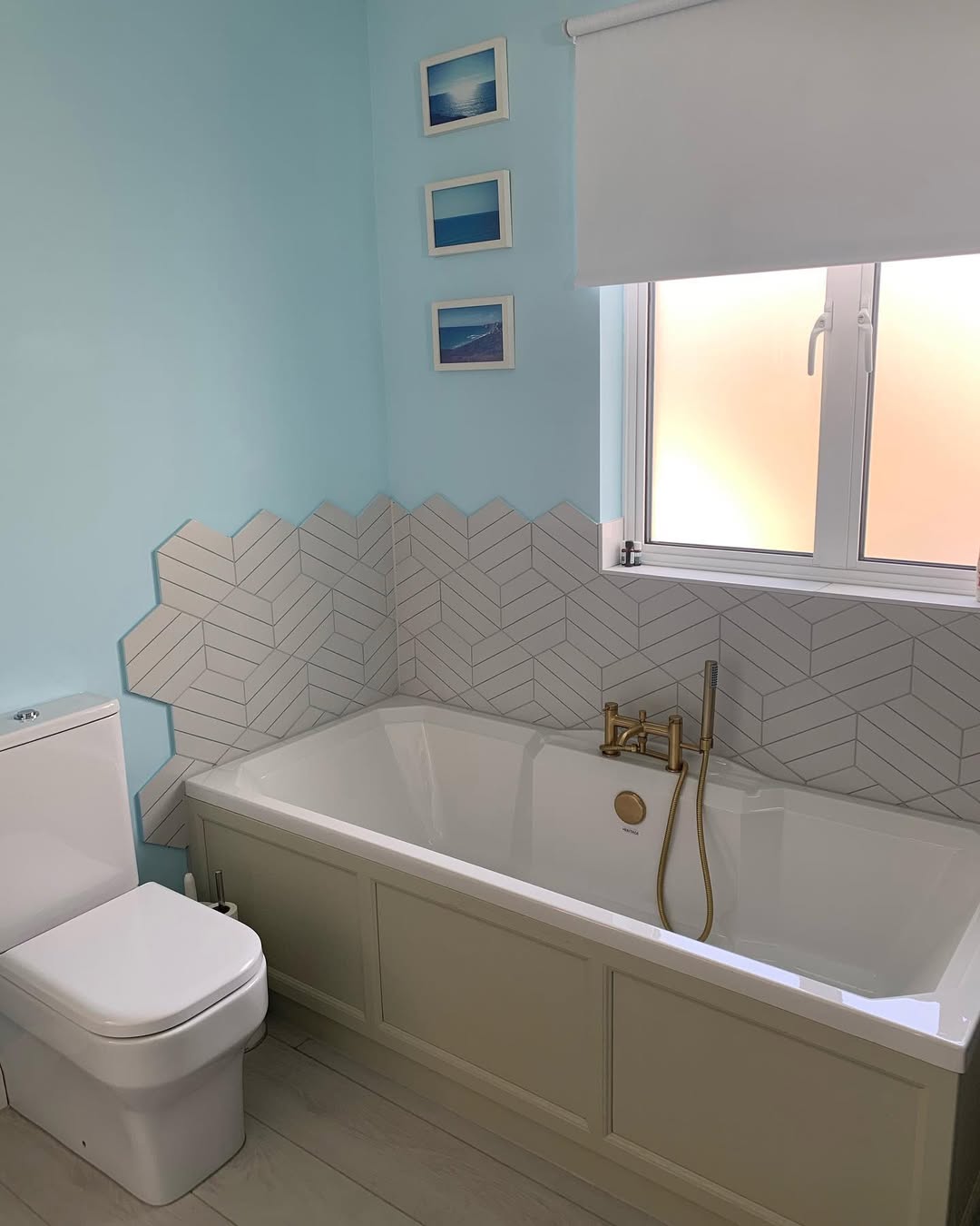 Family bathroom with light blue walls, herringbone chevron tiles, freestanding bathtub, and brass fittings