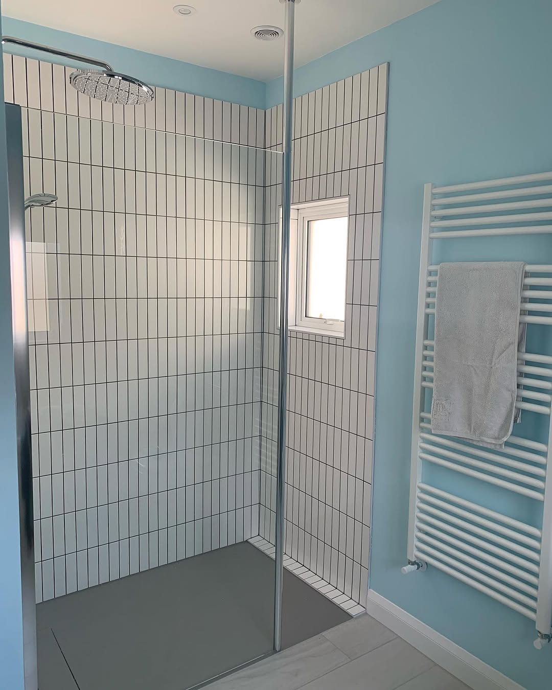 Walk-in shower with vertical white tiles and chrome rainfall head in light blue bathroom