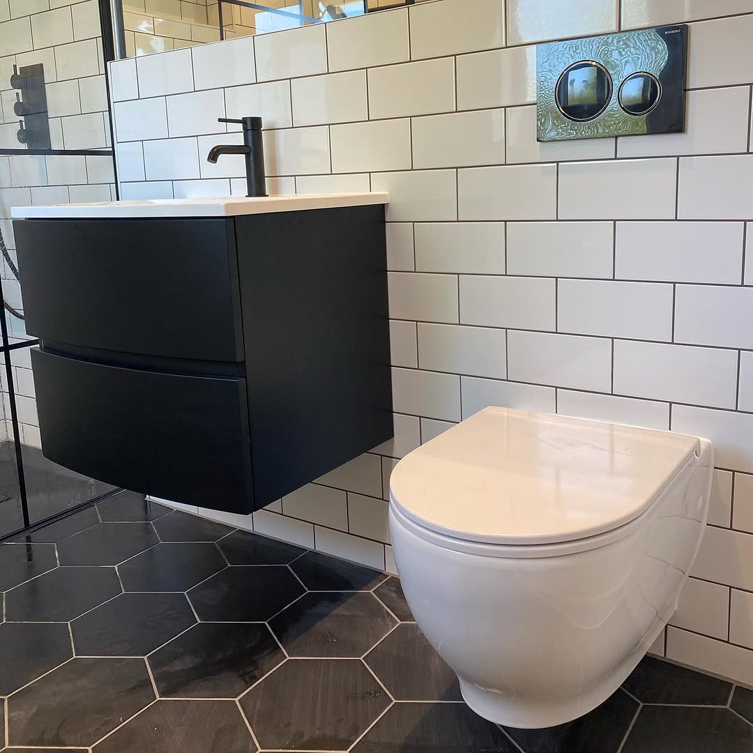 Wall-hung toilet with black flush plate and floating vanity with black tap against white metro tiles