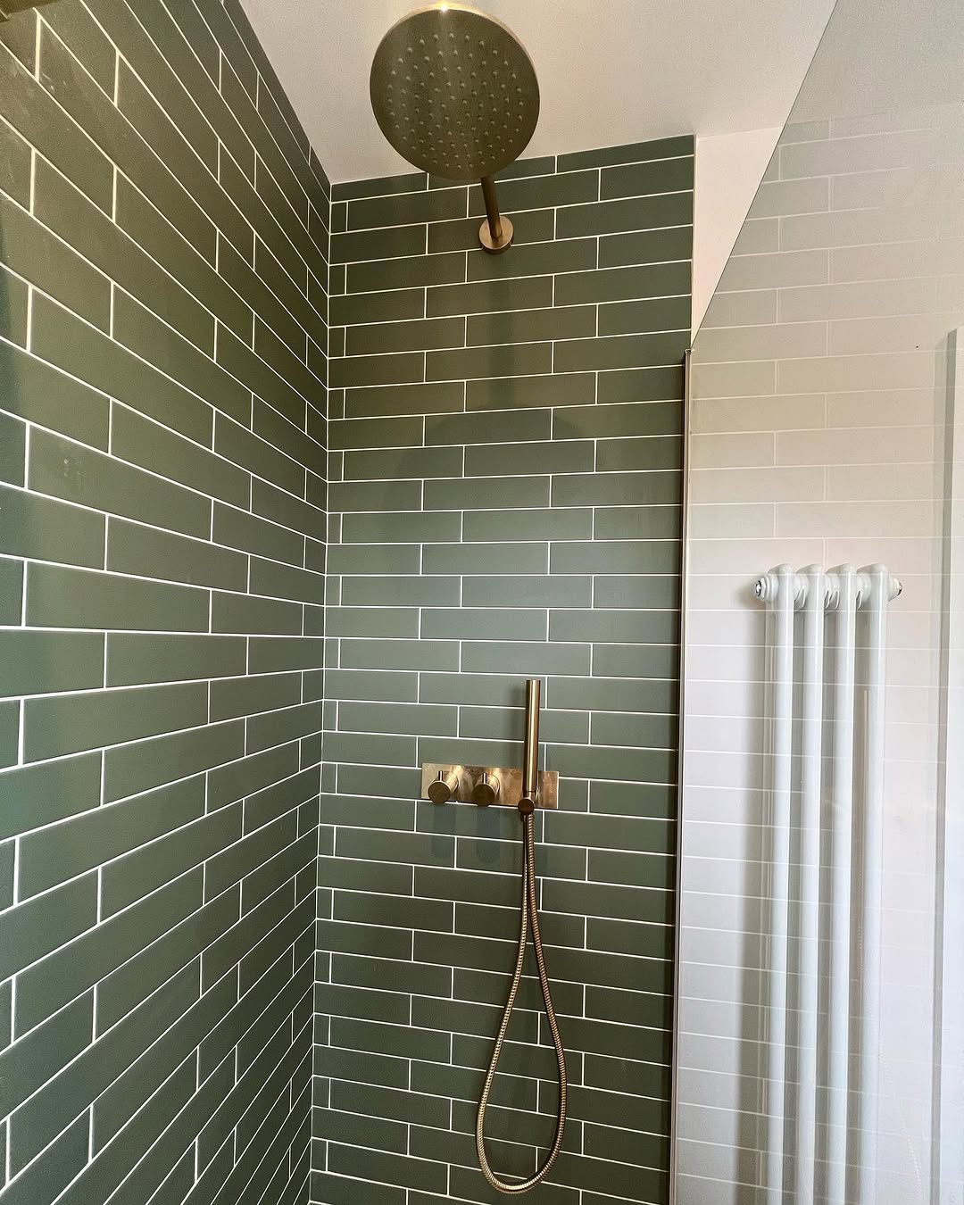 Walk-in shower area with sage green subway tiles and brushed gold rainfall and hand shower fixtures